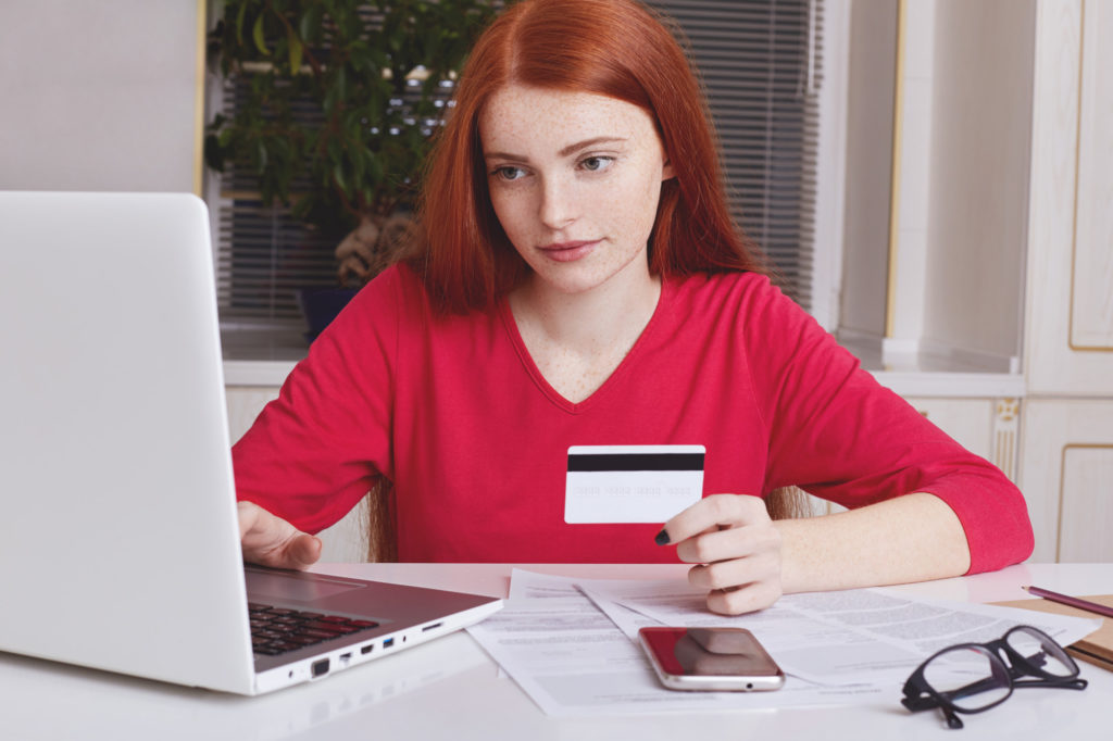 serious-freckled-ginger-female-uses-laptop-computer-e-commerce